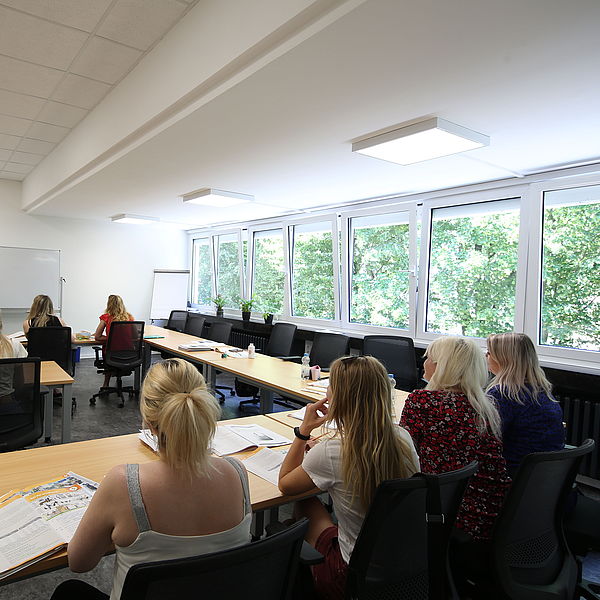 Klassenzimmer mit mehreren Frauen, die einem Dozenten zuhören, der vor einer weißen Tafel steht und erklärt.