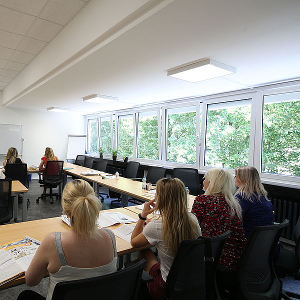 Klassenzimmer mit mehreren Frauen, die einem Dozenten zuhören, der vor einer weißen Tafel steht und erklärt.