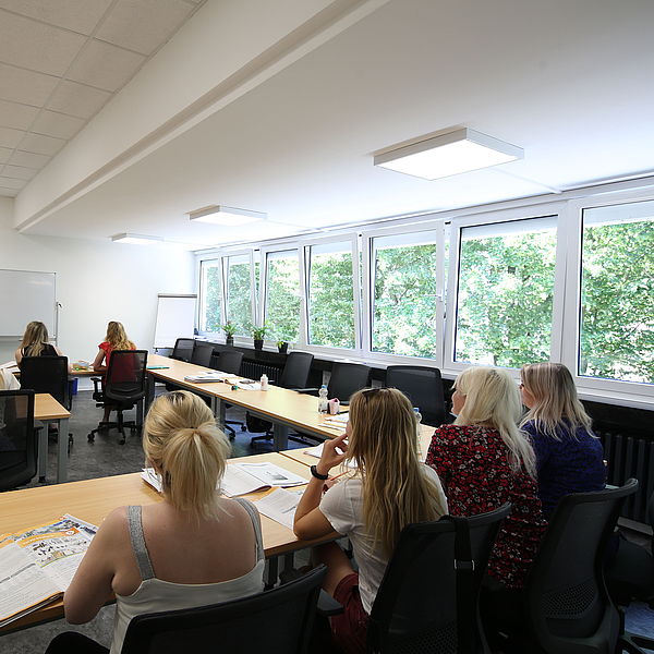 Klassenzimmer mit mehreren Frauen, die einem Dozenten zuhören, der vor einer weißen Tafel steht und erklärt.
