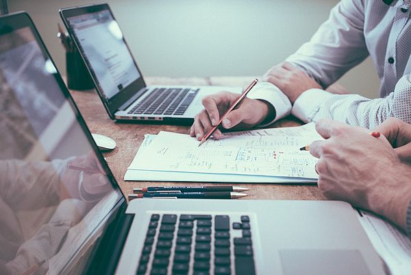 Zwei Personen arbeiten gemeinsam an einem Schreibtisch mit Notizen und zwei geöffneten Laptops.