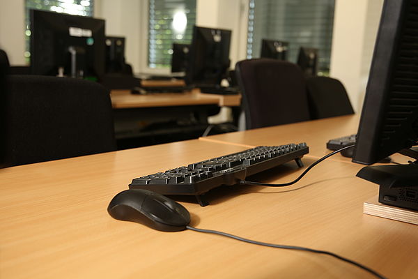 Leerer Computerarbeitsplatz mit Tastatur, Maus und Monitor in einem Büro mit mehreren Arbeitsplätzen.