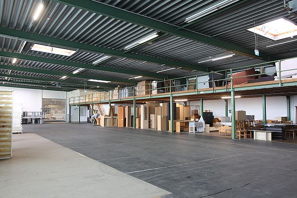 Großes halbleeres Lager mit Holzmöbeln und Kartons auf Regalen im hinteren Teil des Lagers.